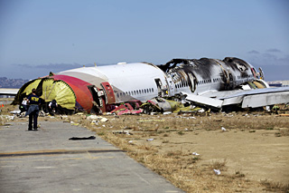 A crash investigator wearing an NTSB shirt approaches the burned-out body of a crashed passenger jet off the end of a runway. A crash investigator wearing an NTSB shirt approaches the burned-out body of a crashed passenger jet off the end of a runway.