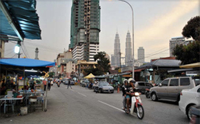 View of a street lined with umbrella stands. Cars and a motorcycle on the street. High-rises in the background.