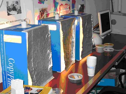 A photo of homemade light houses made from cardboard boxes, aluminum foil, and fluorescent lights.