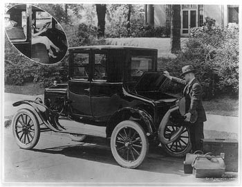 Man loading luggage into the trunk of a Ford coupe; insert of a woman seated behind steering wheel. c1923.