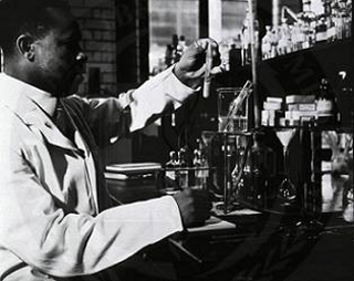 A lab worker examines a blood sample (grayscale photograph).