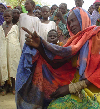 A woman in front of a crowd of kids is point to something while sitting down with her wrapped broken wrist. A woman in front of a crowd of kids is point to something while sitting down with her wrapped broken wrist.